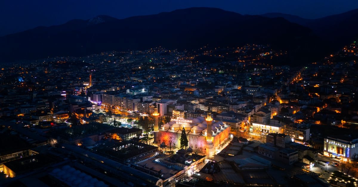Stunning night aerial view of Bursa city with illuminated mosque and vibrant city lights.