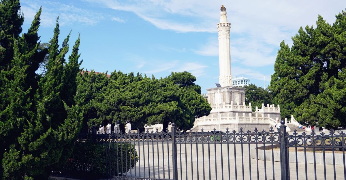 Anshan Travel Guide: Iron City Roots and Northeastern Rhythm A striking white monument stands tall behind a decorative iron fence in a lush green park setting.