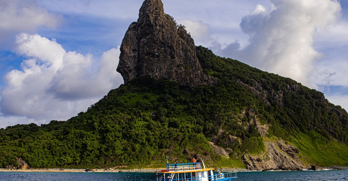 Adamstown, Pitcairn Travel Guide A vibrant boat sails by a stunning rocky island with lush greenery under a dramatic sky.