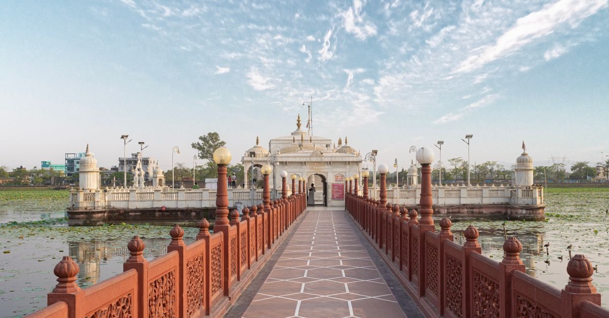 Peaceful scene of a historic Jain temple in Varanasi, India, surrounded by water and clear sky.