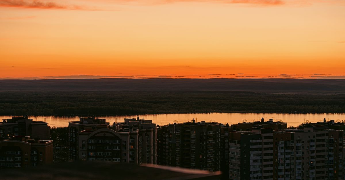Slow Mornings in Ufa: A Quiet Travel Guide to Bashkortostan's Capital City skyline at sunset with vibrant orange hues and silhouetted high-rises by a river.