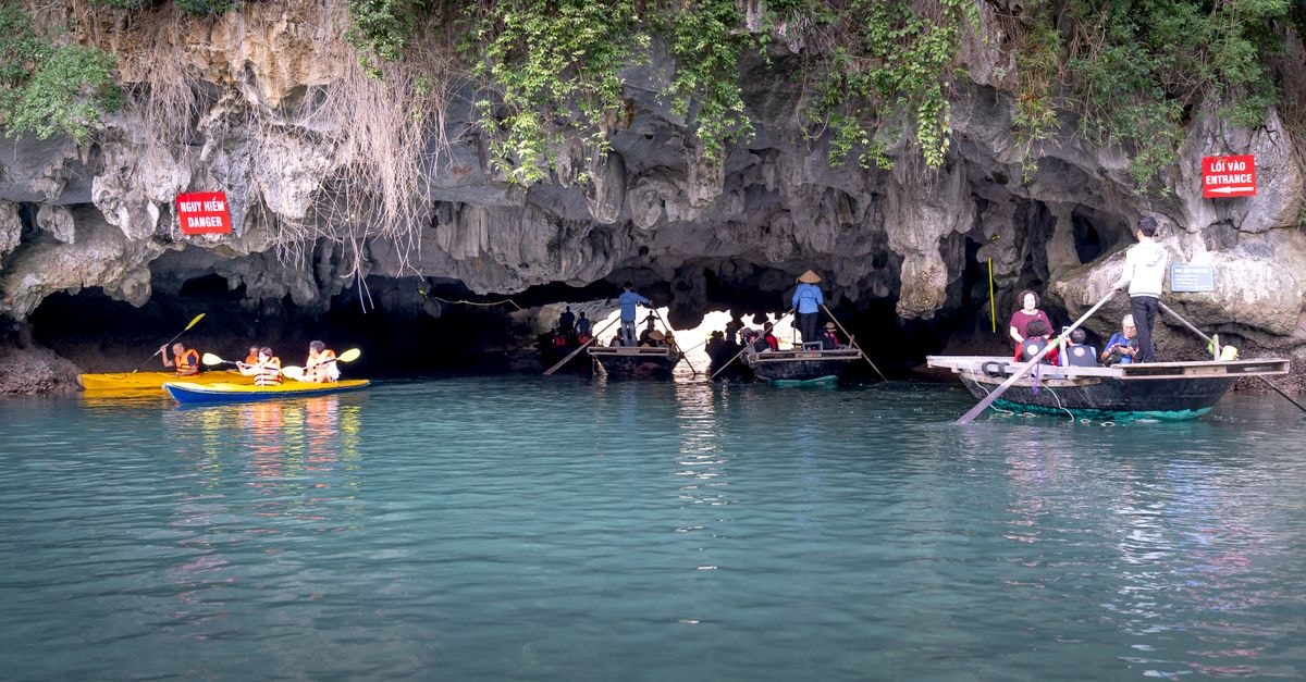 A Quiet Coastal Discovery: Sumbe Travel Guide Kayakers and tourists navigate through a picturesque limestone cave entrance on a tranquil day.
