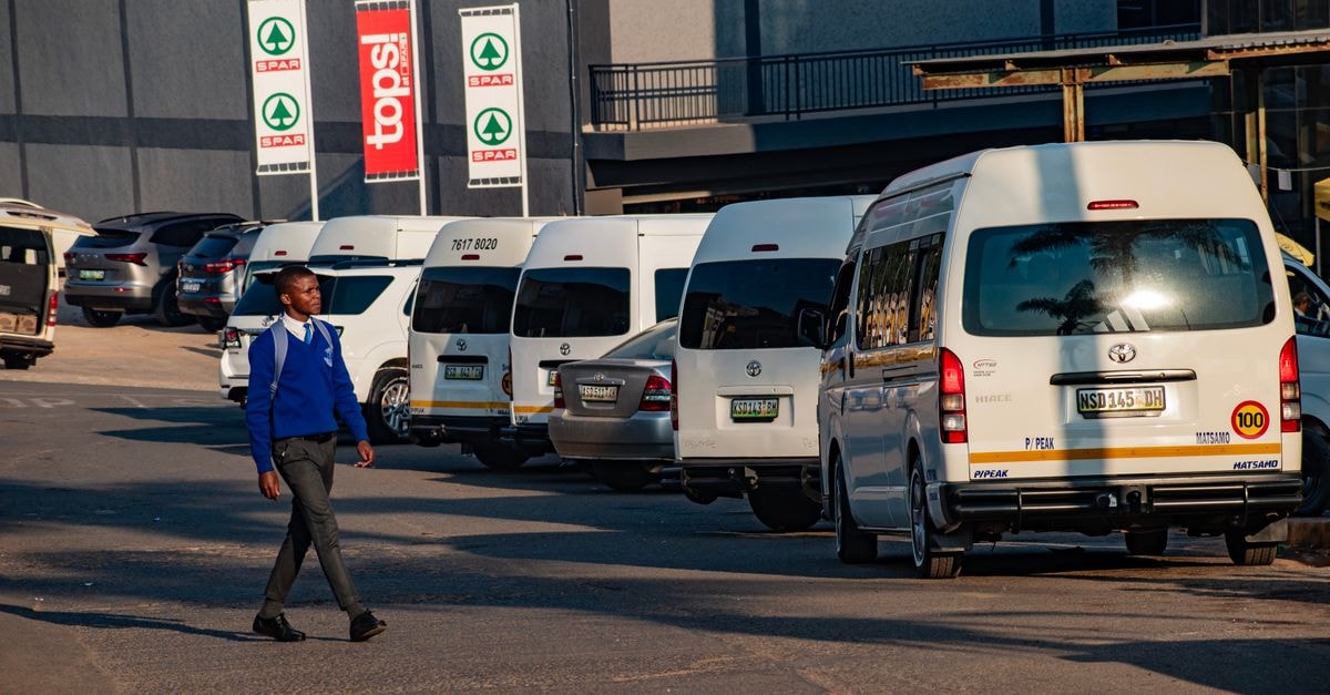 A Central Address in Manzini, Eswatini: City Setting and Surrounding Eateries A man walks by a row of parked minibuses in Manzini, Eswatini.