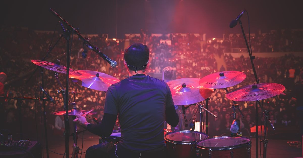 Back view of drummer playing on stage at a live music concert with a packed audience.
