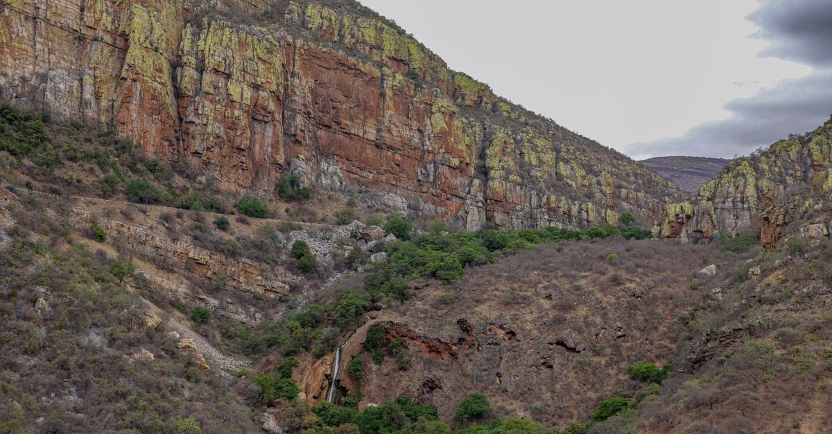 A breathtaking view of a rocky canyon with lush green patches and towering cliffs, showcasing nature's raw beauty.