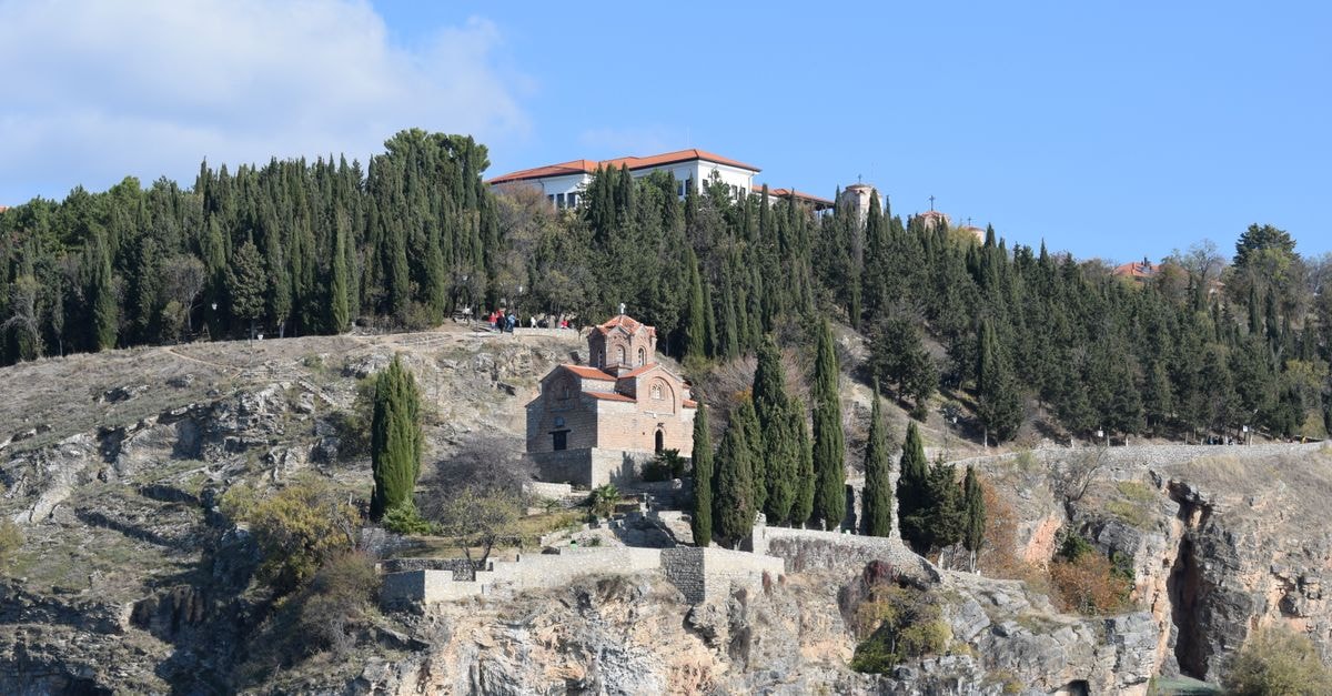 Beautiful view of a historic church perched on a rocky hill with cypress trees, overlooking Lake Ohrid.