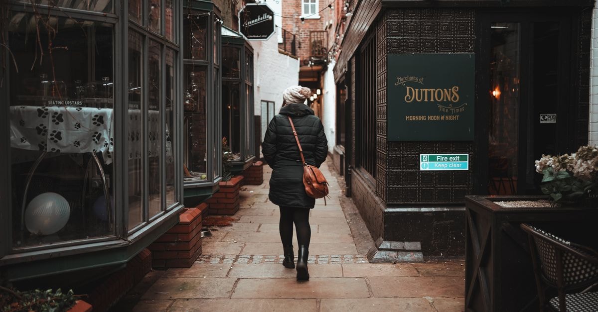 A lone woman walks through a quaint urban alley lined with shops, creating a cozy atmosphere.