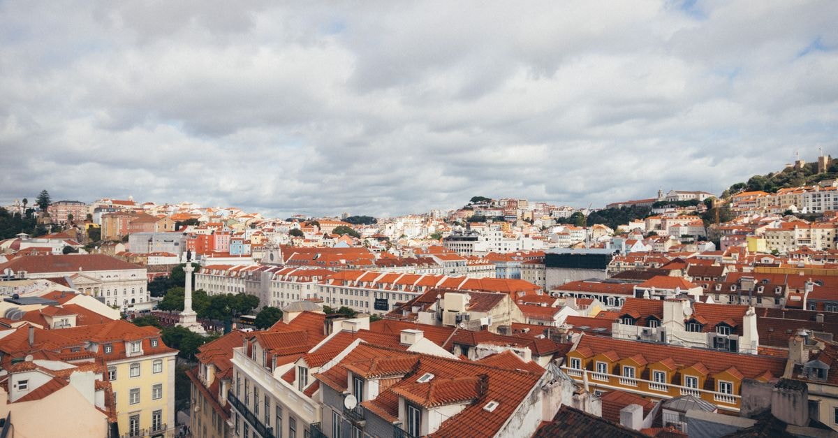 A picturesque aerial view of Lisbon, showcasing its iconic red rooftops and historic architecture on a cloudy day.