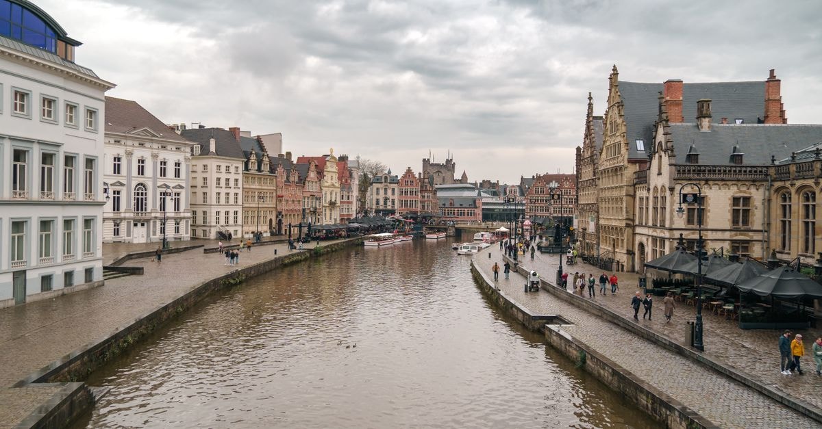 Charming canal scene in Ghent, Belgium with historical architecture on a cloudy day.