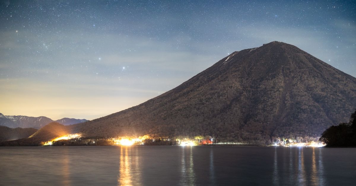 Nikko Travel Guide: A Calm Escape Into Japan's Historic Mountains Serene view of Mount Nantai under a starlit sky by Lake Chuzenji in Nikko, Japan.
