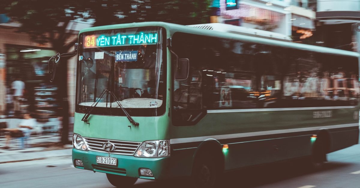 Sonsonate Travel Guide: Buses, Bites, and Local Rhythm Green Hyundai bus on a bustling urban street in Vietnam, showcasing city life.