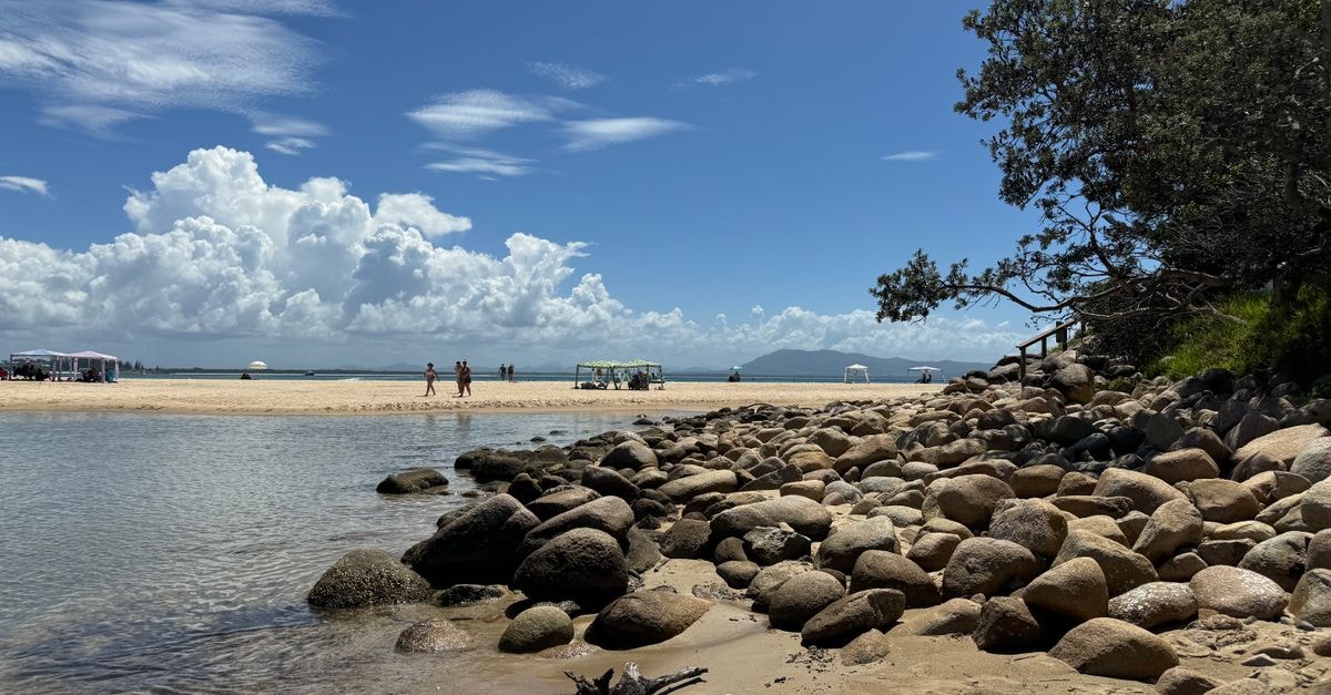 Serene coastal view with rocks, trees, and people under blue skies.