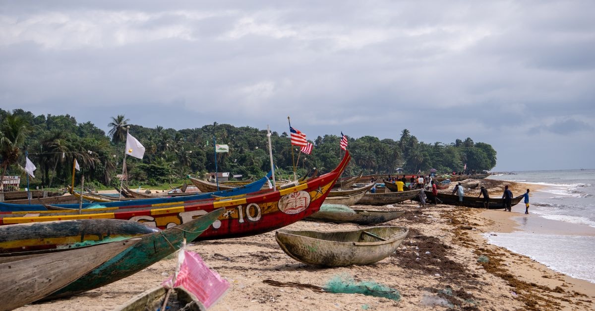 Colorful wooden fishing boats line the sandy beach in Robertsport, Liberia, amidst a vibrant coastal village scene.