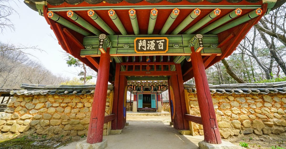 Gimhae Travel Guide: Ancient Gaya History Meets Quiet Local Flavor A vibrant Korean temple gate with intricate design, framed by stone walls and trees.