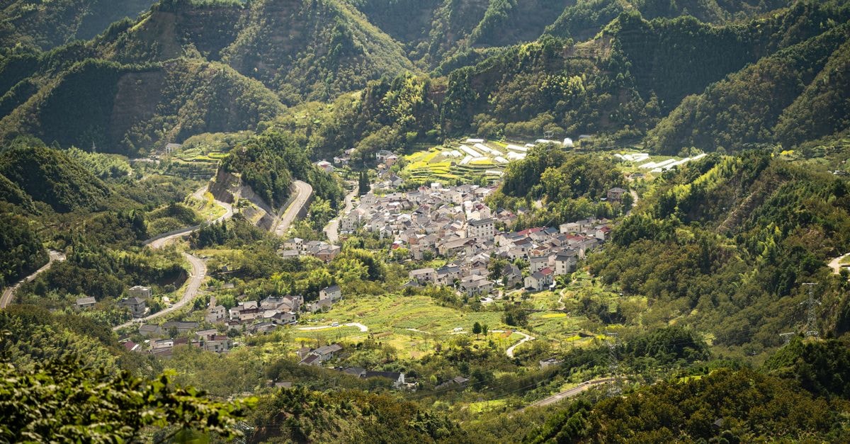 Huludao Travel Guide: Planning Tips, Costs and Things to Do A breathtaking aerial shot of a quaint village nestled among lush green mountains on a sunny day.