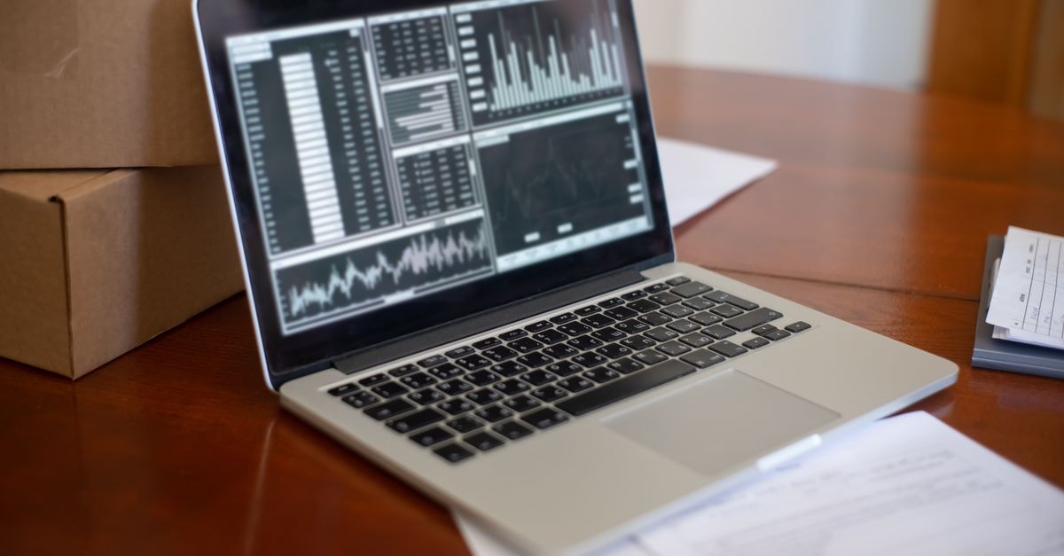 Laptop showing data graphs on wooden table with cardboard boxes, depicting a small business office setting.