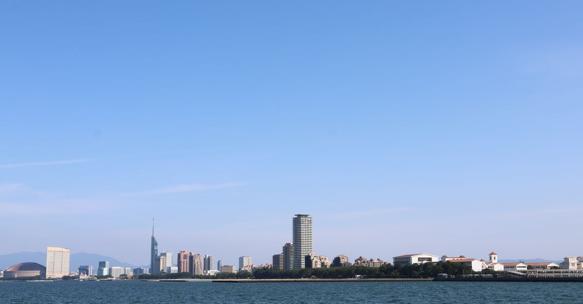 Panoramic skyline of Fukuoka City featuring iconic buildings along the waterfront under a clear blue sky.