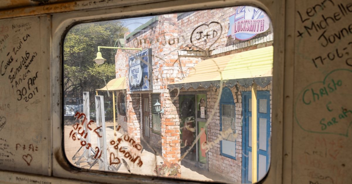 Soshanguve Travel Guide: Getting Around and Eating Well View through graffiti-marked train window showing rustic locksmith shop facade.