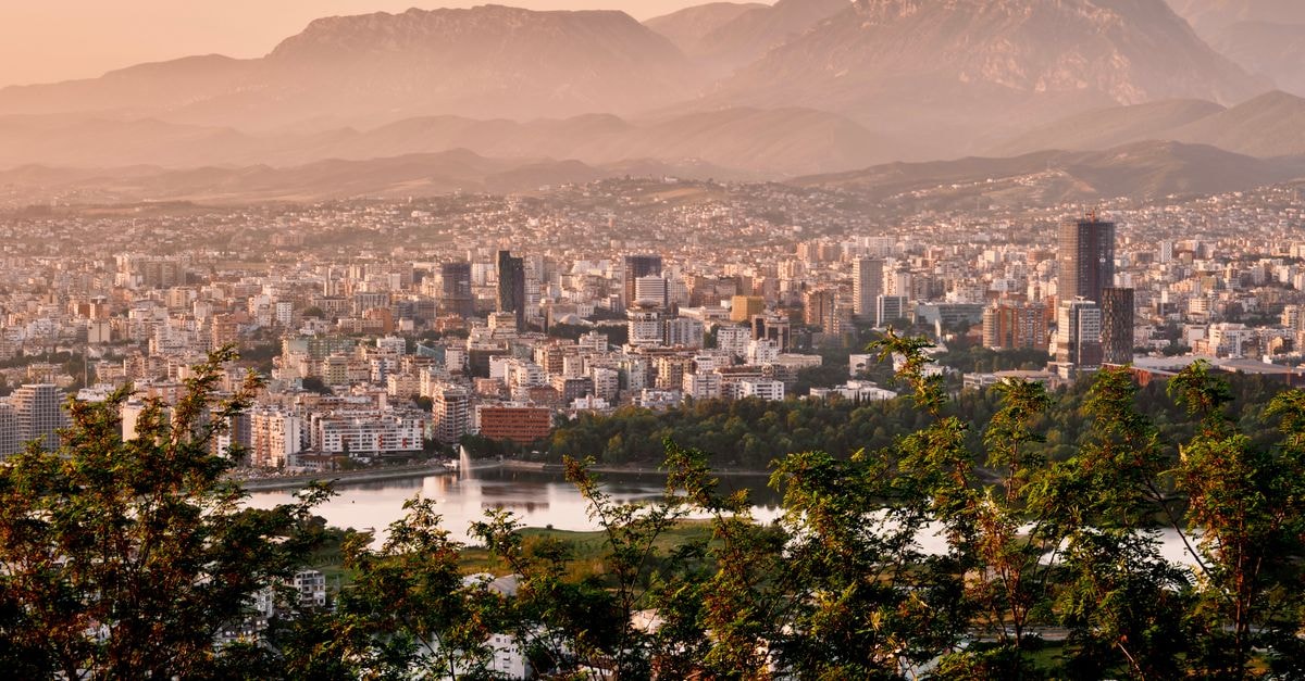 A stunning aerial view of Tirana's skyline framed by mountains and lush greenery during sunset.