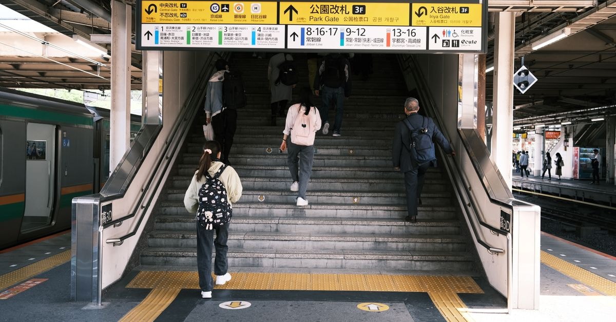 People ascending stairs at a Tokyo railway station, emphasizing city life and public transportation.