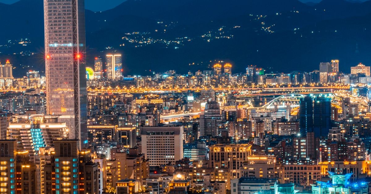 A breathtaking aerial view of a city skyline at night with illuminated skyscrapers and mountains in the background.