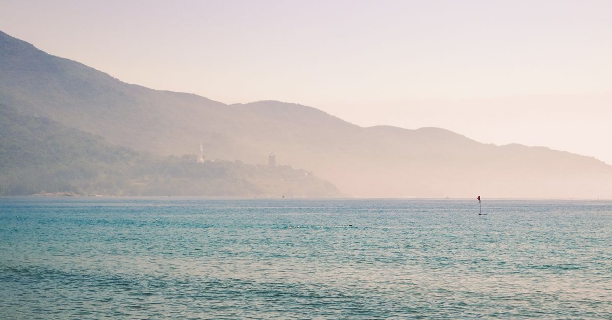 Dili Travel Guide: Tropical Mornings, Microlets and Ocean Flavors Peaceful scene of Vietnam's coastline with mountains in the background, captured at sunrise.