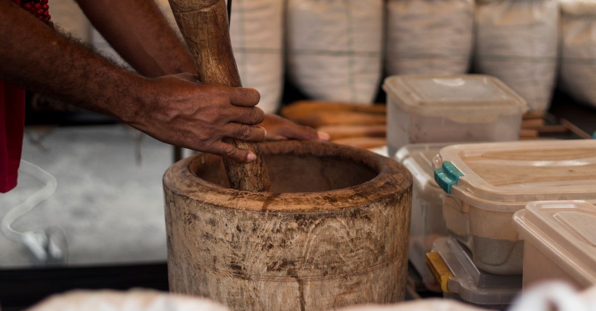 Honiara Travel Guide: History, Markets and Coastal Flavors Close-up of hands grinding herbs in a wooden mortar at a São Paulo market stall.