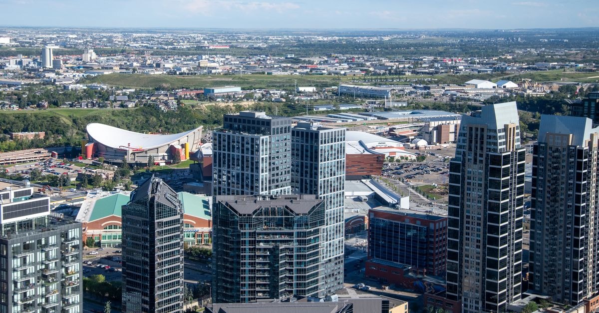 The Explorer Hotel in Yellowknife: Aurora Views on 49th Avenue Aerial view of Calgary cityscape featuring modern skyscrapers and the iconic Saddledome under a clear blue sky.