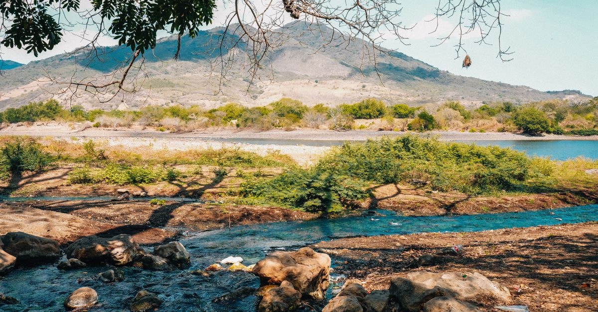 A tranquil river flows through lush greenery with a backdrop of mountains in El Salvador's picturesque scenery.