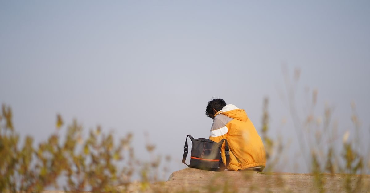 Hotel in Bihar Sharif: A Practical Base in a Historic Smart City A man in a yellow jacket sitting on a cliff in Bihar Sharif, India, with a serene blue sky.