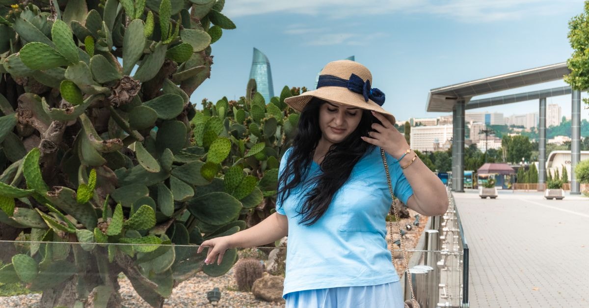 Caucasian woman in straw hat strolling through Baku's serene promenade with cityscape in background.