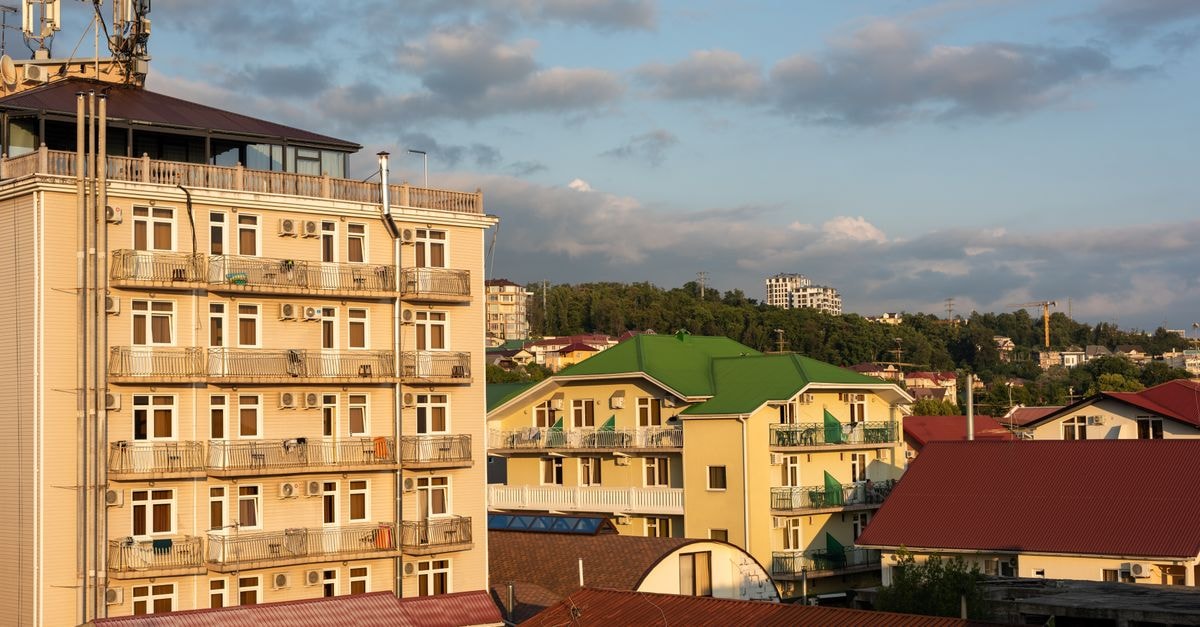 View of urban buildings at sunset with a hilly backdrop and cloud-filled sky.