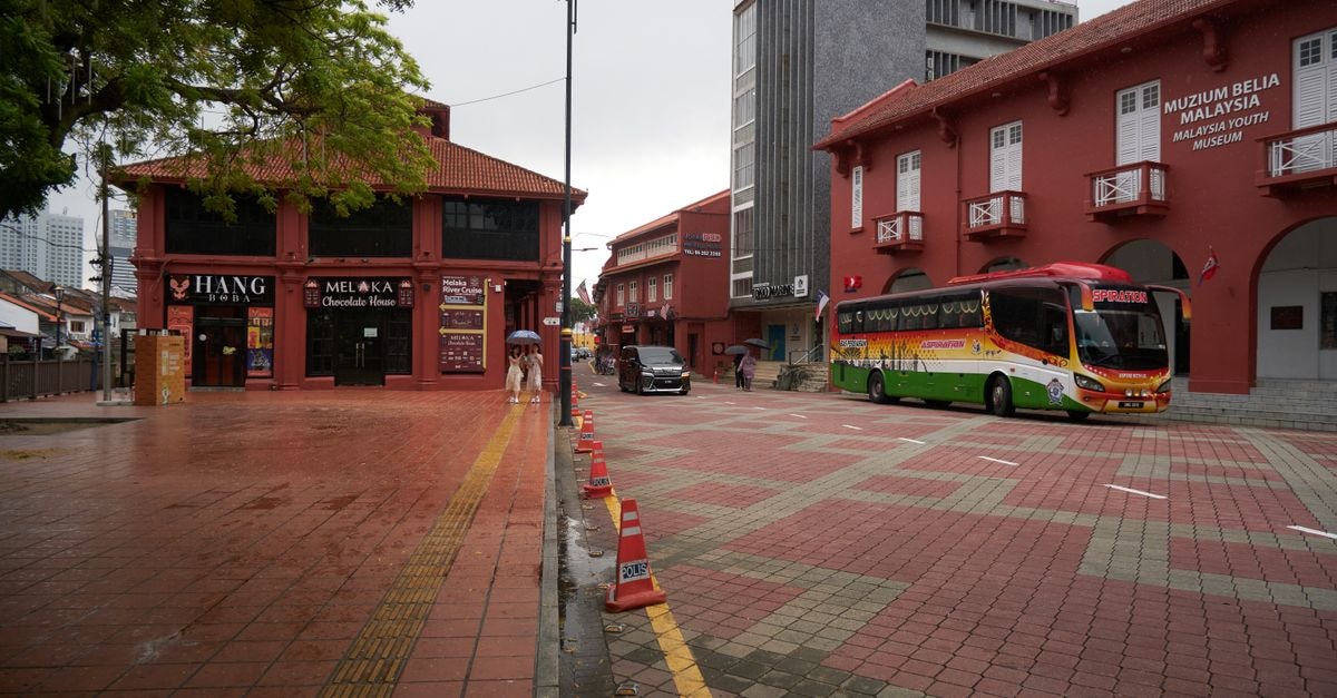 Malacca Travel Guide: Planning Tips, Costs and Things to Do City street scene in Malacca featuring red brick buildings and a colorful bus on an overcast day.