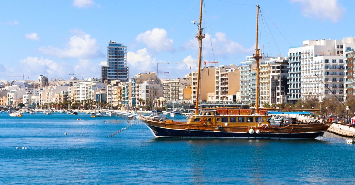 Sliema Travel Guide: Seafront Strolls, Local Plates Charming sailboat anchored in Sliema, Malta with modern cityscape and clear blue water.