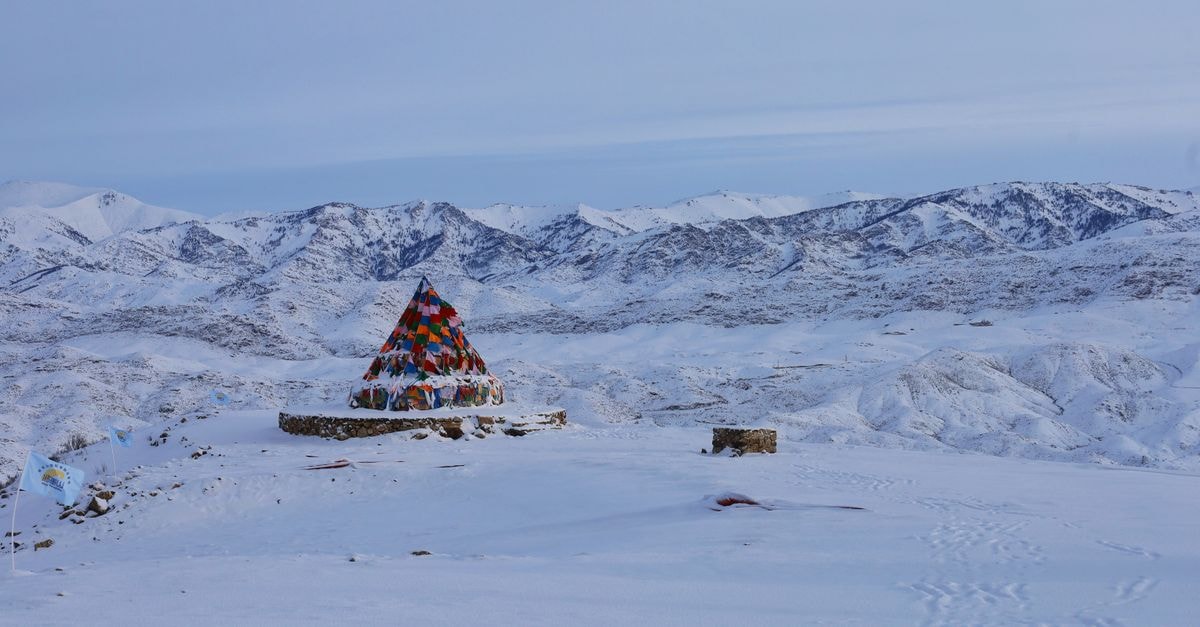 A vibrant tent amidst snow-covered mountains offers a striking contrast in a serene winter setting.