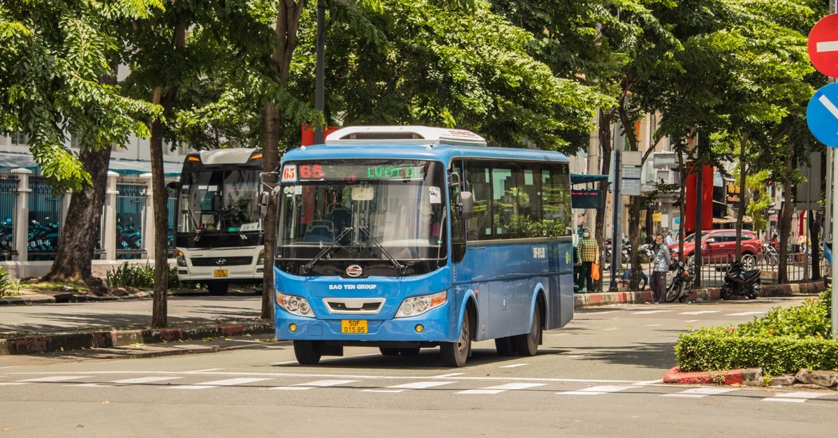 Salem travel guide: bus routes and local food, slowly Blue bus navigating the streets of Hồ Chí Minh City, Vietnam, surrounded by urban greenery.