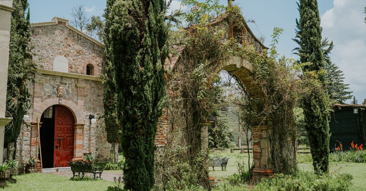 Tulcán Travel Guide: Topiary Cypresses and Andean Border Charm Beautiful view of a historic stone church and ivy-covered arch surrounded by lush greenery.