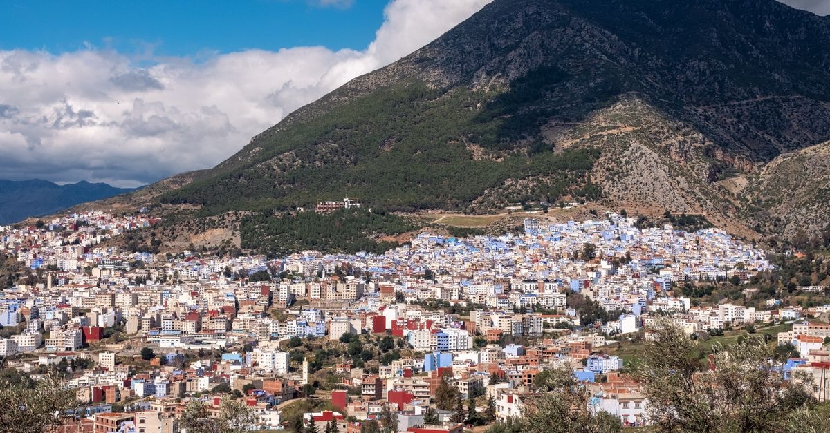 Panoramic view of the vibrant blue city of Chefchaouen in Morocco under a dramatic sky.