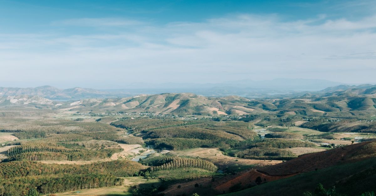 Expansive aerial view of Kon Tum's rolling hills and lush valleys under a clear blue sky.