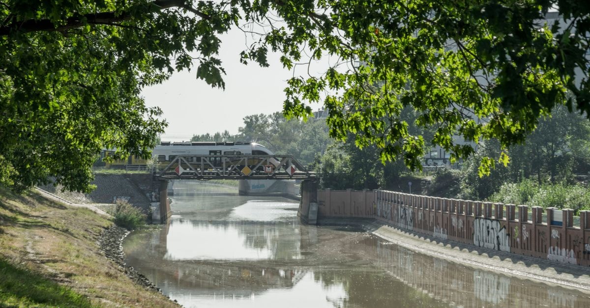 Picturesque view of a train crossing a bridge over a river in lush greenery, Wrocław, Poland.