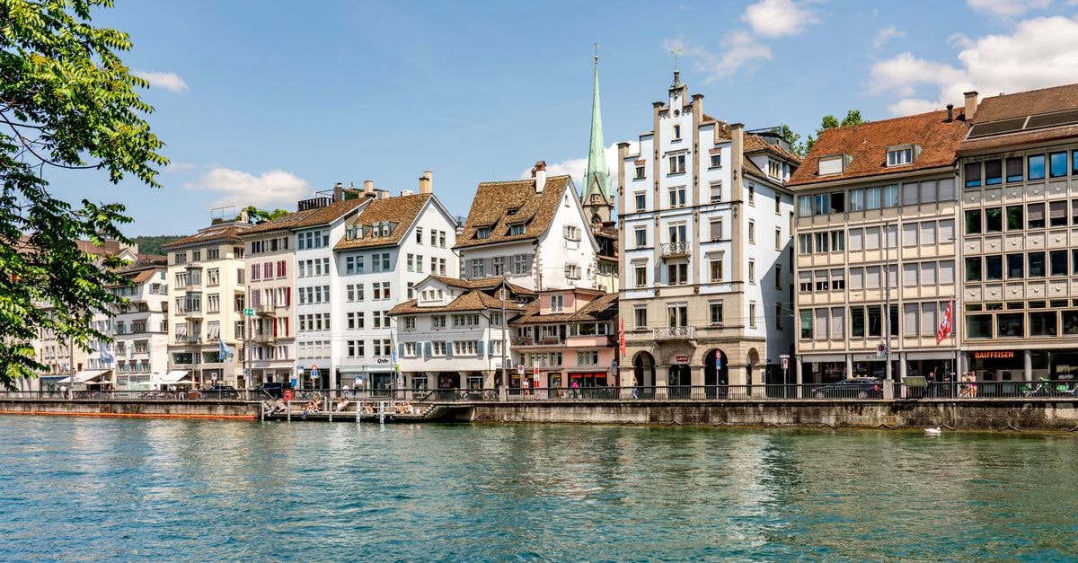 Zurich travel guide: a waterfront city of old town charm Scenic view of Zurich's historic waterfront buildings along the Limmat River on a sunny day.