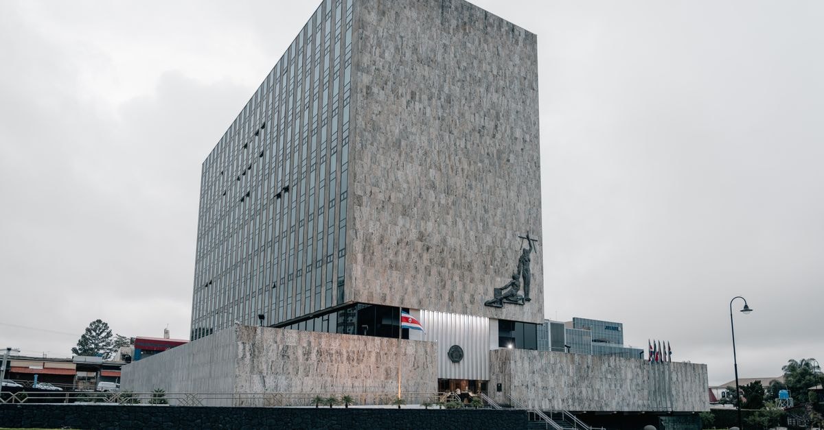 NHC: Established Operator With Stretched Valuation Architectural photo of the Supreme Court building in San José, Costa Rica featuring modern design and national flags.