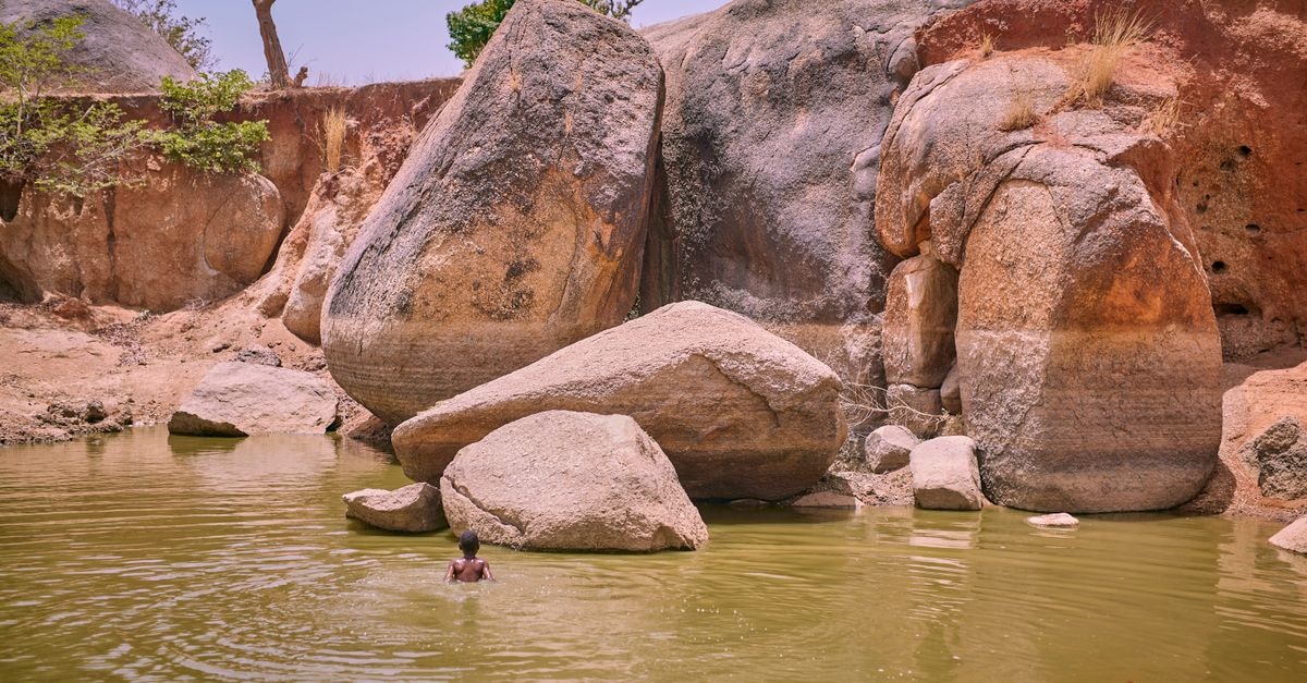 A lone swimmer enjoys a tranquil swim in a rocky desert oasis under clear skies.
