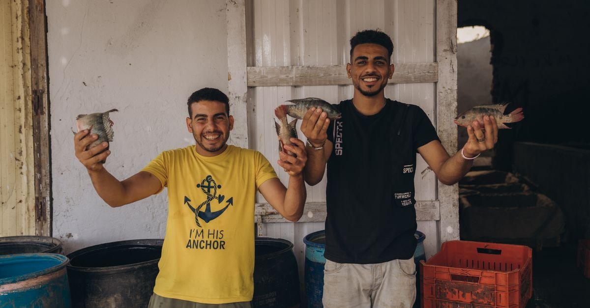 Aqaba Travel Guide: Fort Walls, Fish Markets, and Red Sea Light Two men proudly holding fresh fish at a local market in Cairo, Egypt.