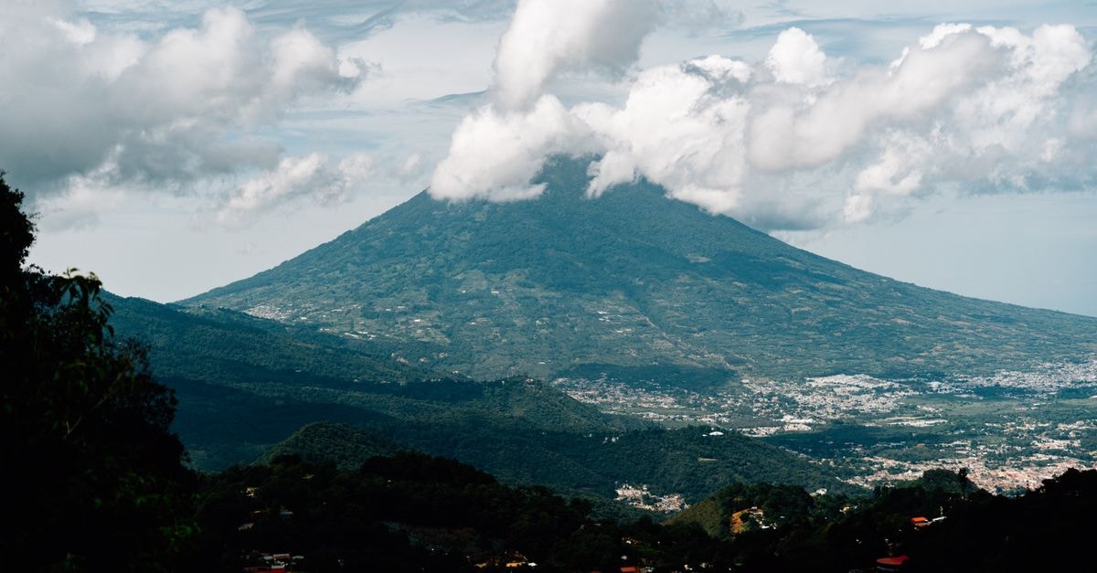 A majestic view of Volcán de Agua in Guatemala under a vibrant sky, surrounded by lush landscape.