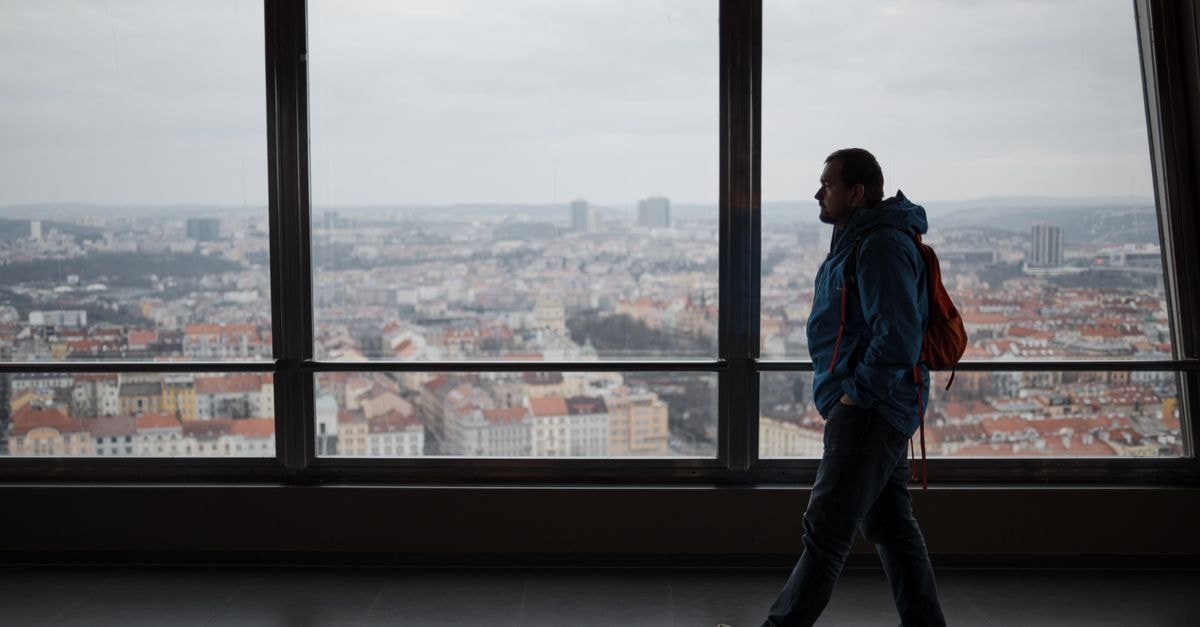 Hôtel Beau Séjour in Man: A Simple Stop on the A7 Full body side view of male with backpack strolling along big windows overlooking cityscape with residential buildings in contemporary house