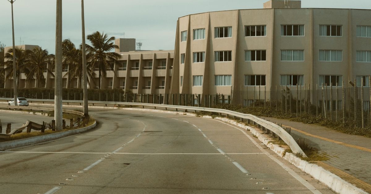 Curved road leading to a modern apartment building in Natal, Brazil, surrounded by palm trees.