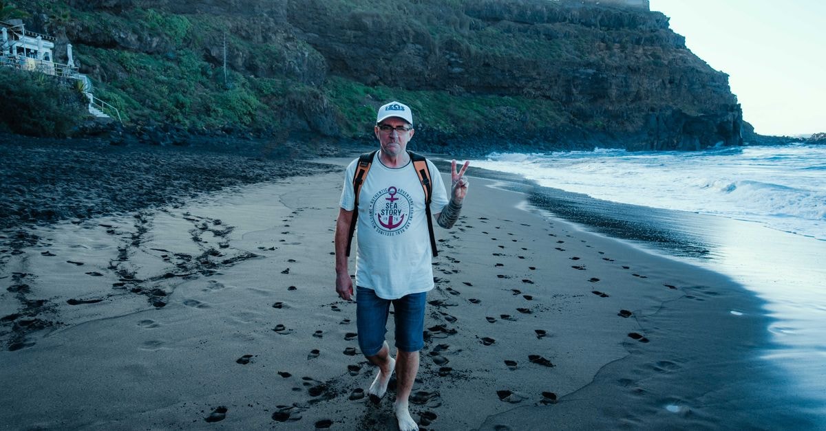 Dennery Travel Guide: Coast, Backpacks and Frigate Birds Casual man walking barefoot on black sand beach making a peace sign gesture.