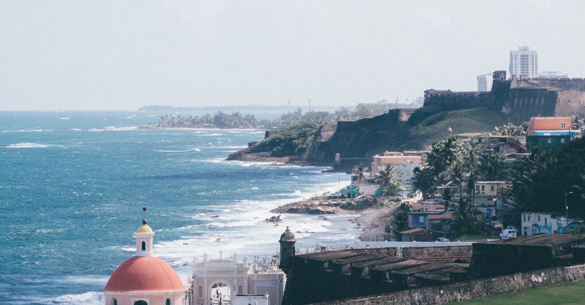 La Guaira Travel Guide: Caribbean Gateway with a Mountain Soul Historic coastal view of San Juan with fortifications and vibrant cityscape by the sea.