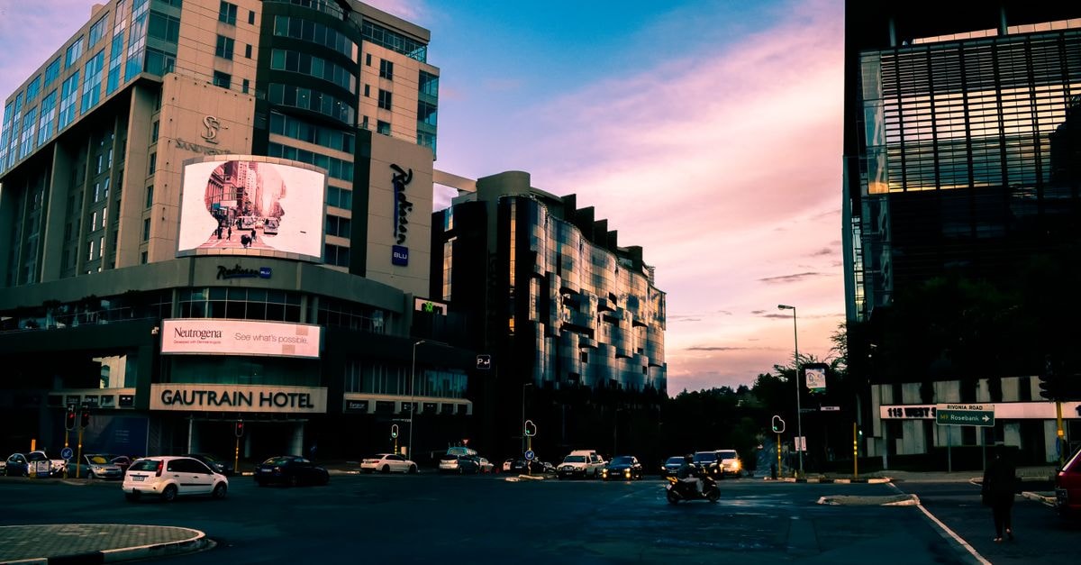Slow Mornings in Lusaka: A Quiet Travel Guide A bustling city street with modern skyscrapers and vehicles at sunset, Gautrain Hotel visible.